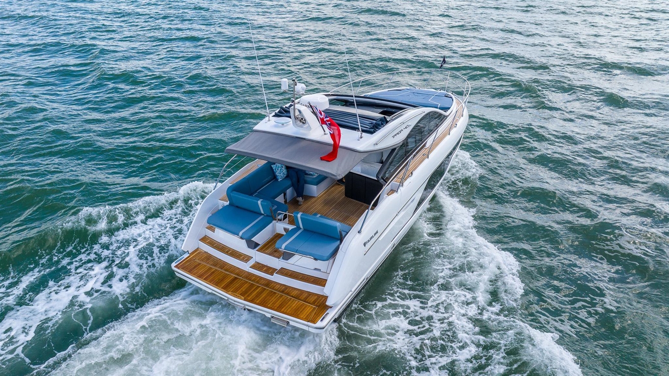 A luxury motor yacht with blue seating and a sunshade glides through turquoise waters, leaving a white wake behind.